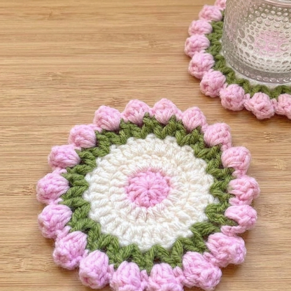 Two crocheted coasters with pink and green patterns on a wooden surface.