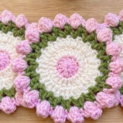 Crocheted coaster with pink and green border on a wooden surface