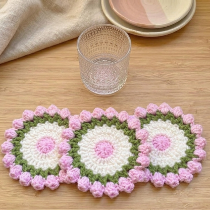 Three crocheted coasters with pink and green patterns on a wooden surface.
