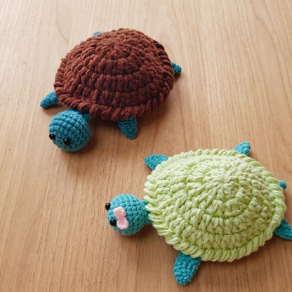 Two crocheted turtle toys, one brown and one green, on a wooden surface.