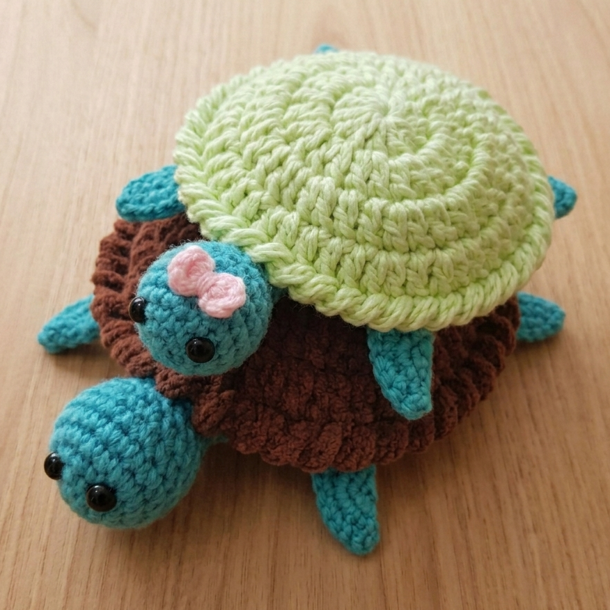 Crocheted turtle toy with a pink bow on a wooden surface